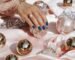Stylish hand showcasing blue nails resting on pink satin surrounded by opulent ornaments and jewelry.