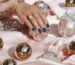 Stylish hand showcasing blue nails resting on pink satin surrounded by opulent ornaments and jewelry.